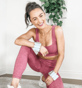 Photo of Megan Roup with hand weights on her wrist wearing her hair up in a ponytail with a pink two-piece workout set on