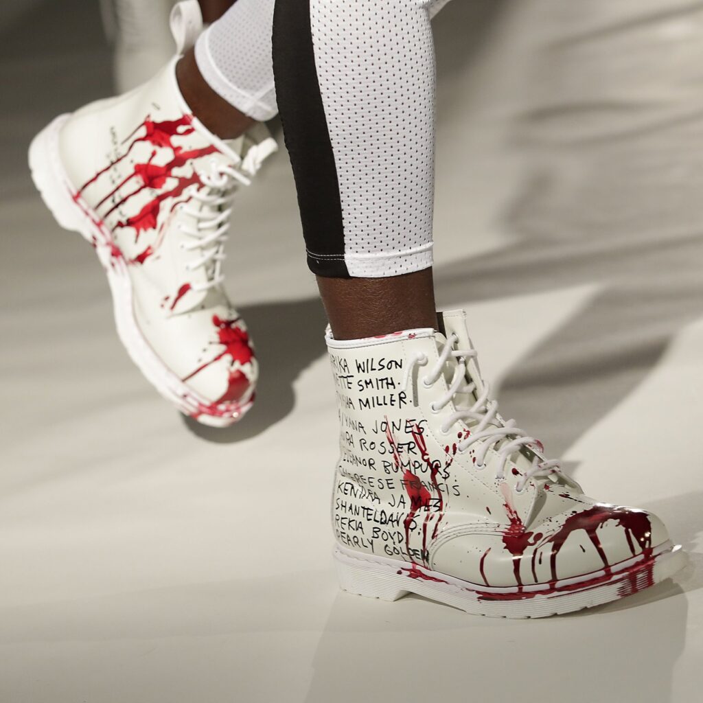 White Pyer Moss shoes with bullet holes and blood next to the names of police brutality victims 