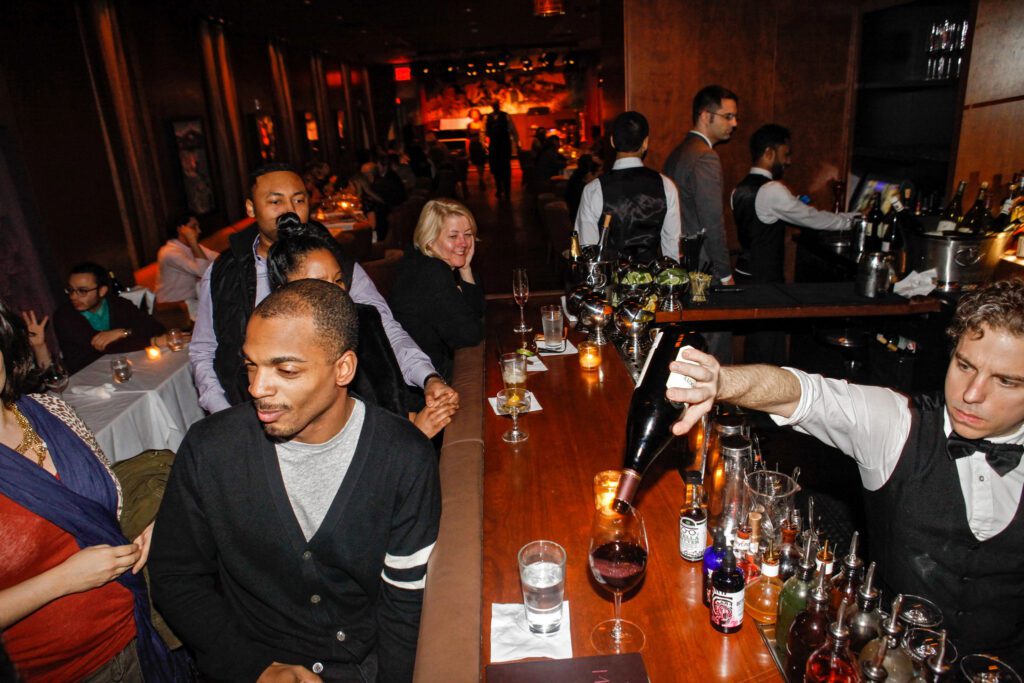 A photo of customers enjoying their time at Minton's Playhouse. Bartender poring a glass of wine.