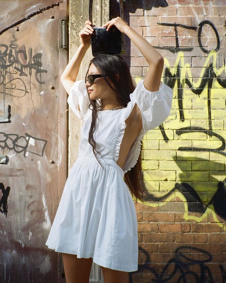 A girl in a ruffled white dress poses while holding a bag over her head. 